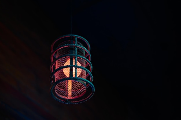 Loft pendant lamp with red blue glow in steel rebar shade wooden interior background copy space