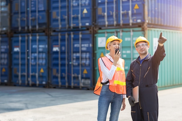 Logistic worker man and woman working team with radio control loading containers at port cargo to trucks for export and import goods.