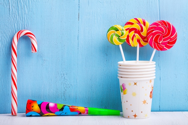 Lollipops in cups with candy cane and whistle on blue wooden wall