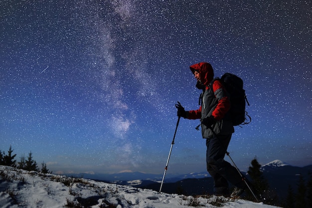 Lone silhouette of adult male hiker on top of snowcapped mountain in anticipation of dawn Starry sky on background