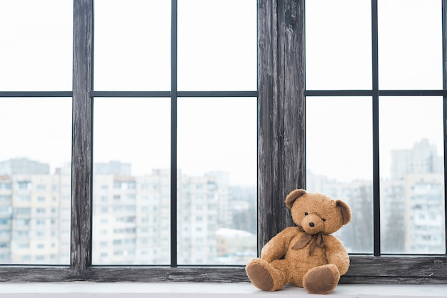 Lone teddy bear sitting near the closed window sill