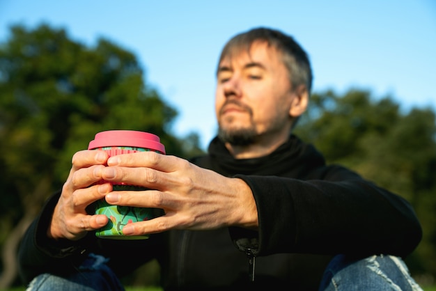 Lonely, alone, single middle aged man drinking coffee in the park. Concept of loneliness, social distancing and self insaltion. Mental health concept, connecting to nature