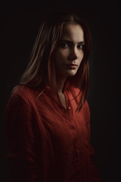 Lonely beautiful woman in coral shirt attentively looking at a camera on dark background