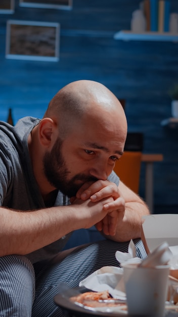 Lonely depressed traumatised man with tears sitting on couch crying feeling exhausted