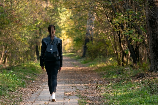 Lonely girl is walking along the alley of the park. Back view. Alone with myself.