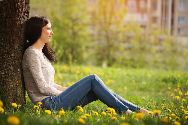 The lonely girl sits at a tree looks in a distance