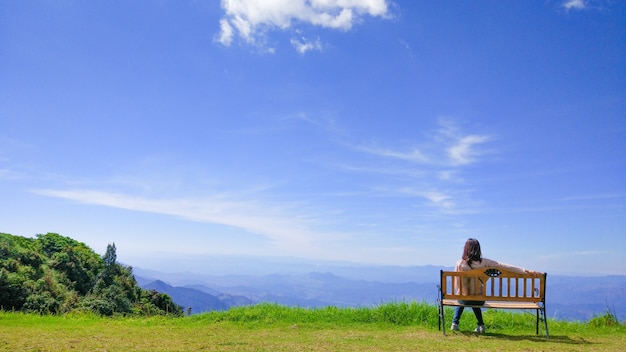 Lonely Girl Sitting On The Bench in garden on mountain and sky scape.