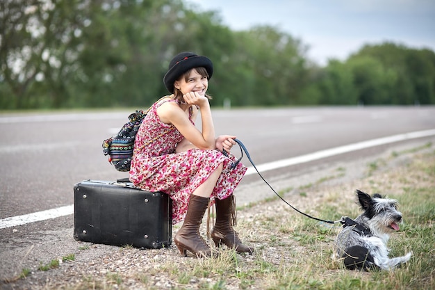 Lonely girl with dog and suitcase standing about road