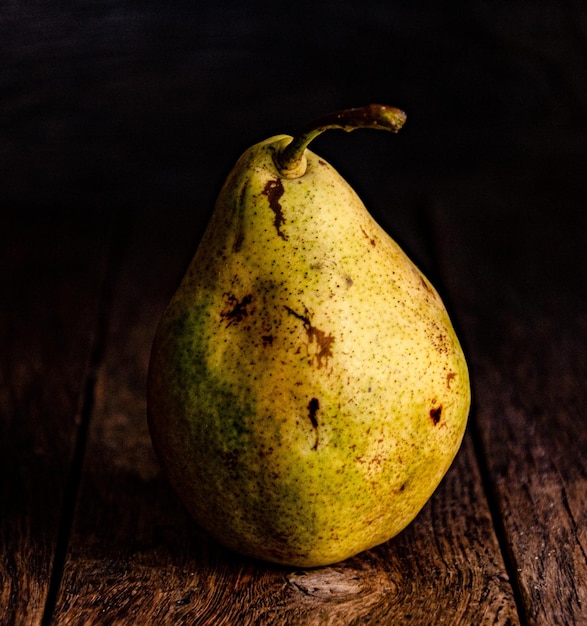 Lonely green pear on a wooden kitchen table against a dark background.