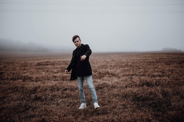 lonely handsome man in a black coat in autumn in a field