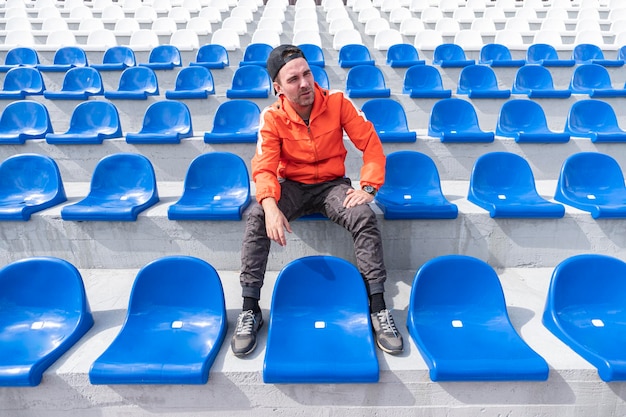 Photo lonely man is sitting and watching a sports competition alone on a large empty grandstand competition and other mass events during the lockdown