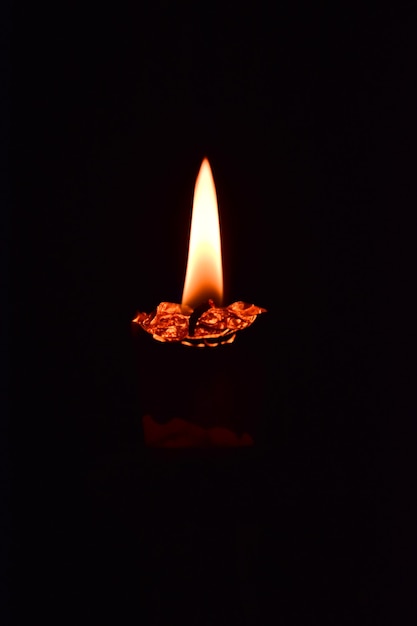 A lonely melted candle burning in the dark. On a dark background. Close-up shot.