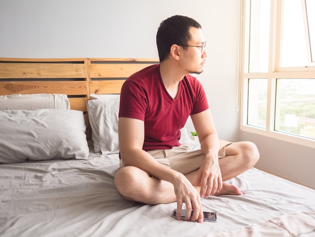 Lonely non-social Asian man with his smartphone in his bedroom apartment.