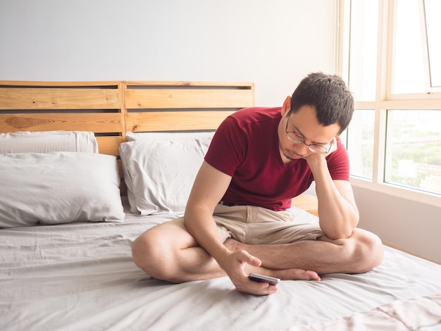 Lonely non-social Asian man with his smartphone in his bedroom apartment.