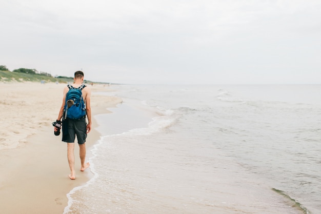 Lonely photographer with a camera in his hand walking along beach