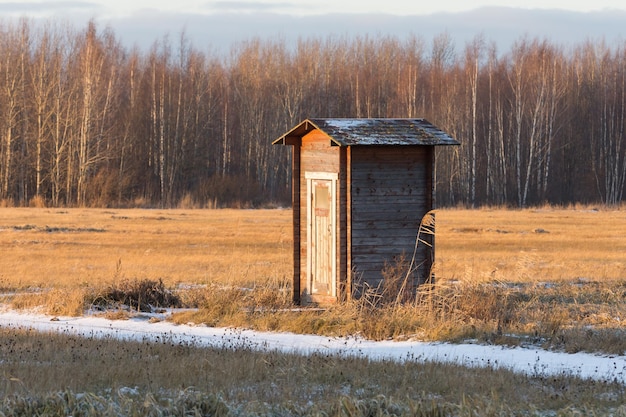 Lonely small building toilet barn in a field against the backdrop of the forest in winter