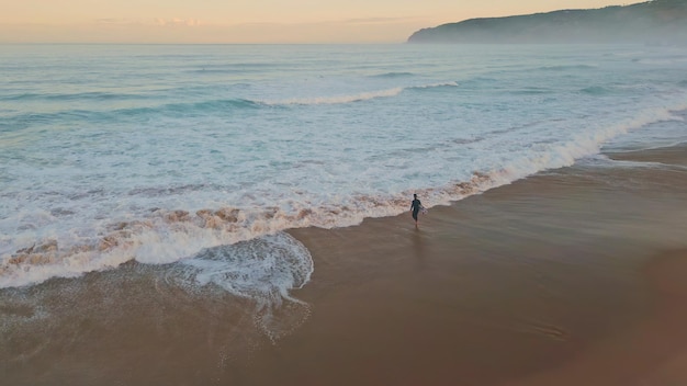 Lonely surfer entering ocean drone shot wonderful pastel sky with marine waves