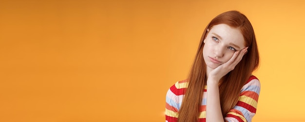 Lonely upset moody cute redhead girlfriend feeling boredom leaning palm look up pouting frowning displeased standing uneasy attend boring meeting staring uninterested reluctant orange background