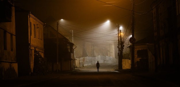 Lonely woman walking in foggy old city with street lights in a coat