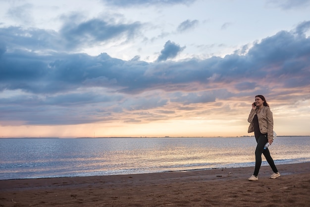 Lonely woman walks on beach at sunset after rain