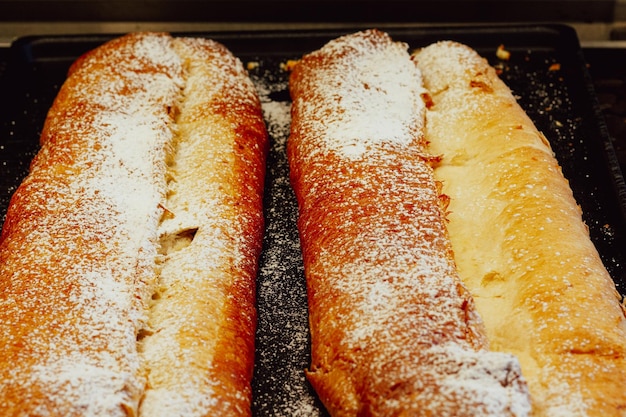 Long apple strudel pies on icing sugar. Bakery sweet dessert on window display