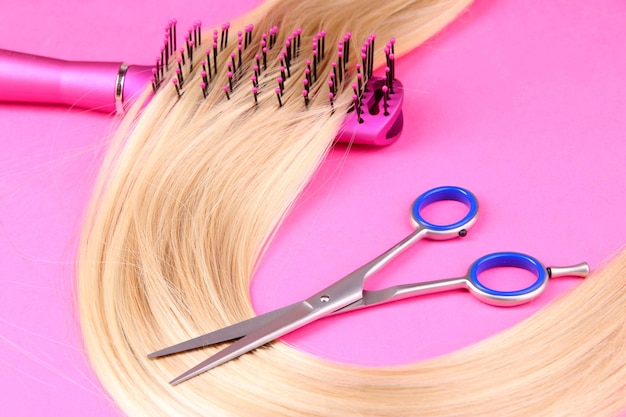 Long blond hair with hairbrush and scissors on pink background