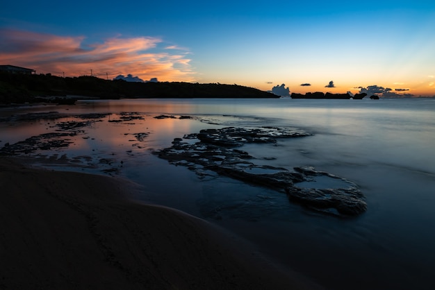 Long exposure at beach after sunset Colorful clouds reflecting on smooth surface sea.