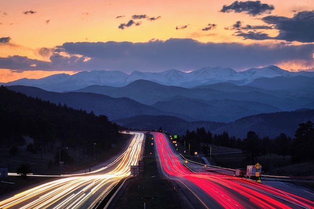 Long-exposure shot of a highway with car lights and a scenic mountainous landscape during sunset