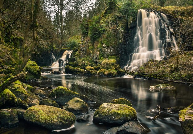 Long exposure shot of Linn Jaw Waterfalls near Livingston Scotland with mossy rocks foreground