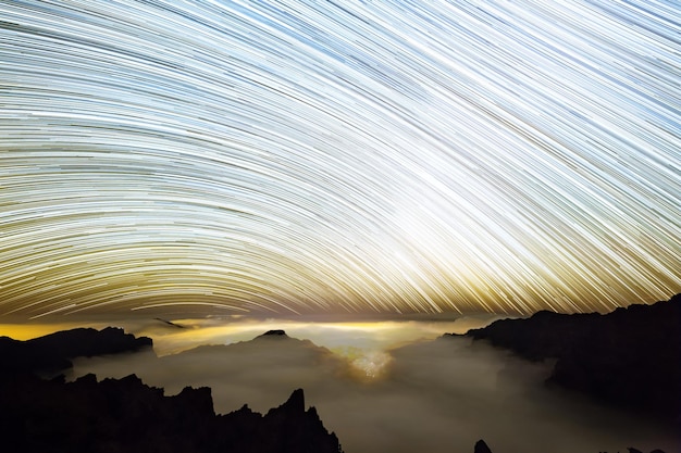 A long exposure of the sky with the stars and the moon in the background.