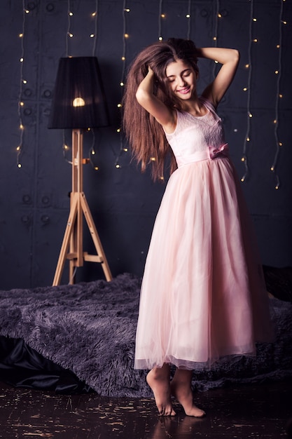 Long-haired girl in pink dress on dark with bokeh