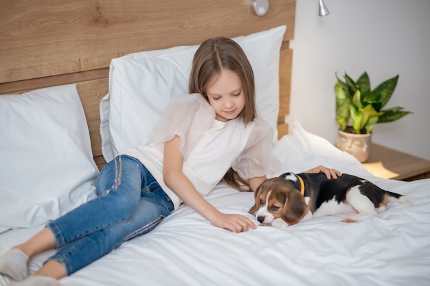 A long-haired girl playing with her puppy on the bed