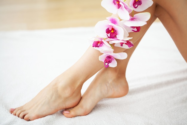 Long legs of a woman with a fresh manicure and orchid flowers.