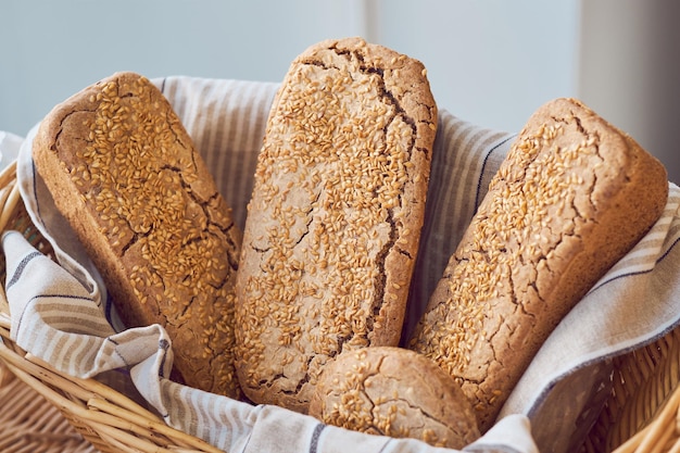 Long loaves of delicious wholegrain bread with sesame seeds in wicker basket placed on table in bakery