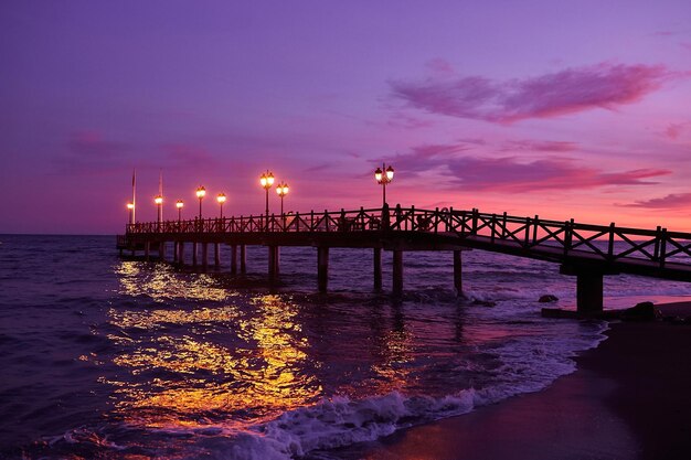 Long pier on the sea in Marbella, Spain at sunset. Illuminated wooden jetty on the beach in Spain