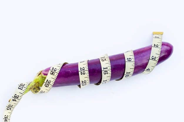 Long purple eggplant wrapped in measuring tape on white background