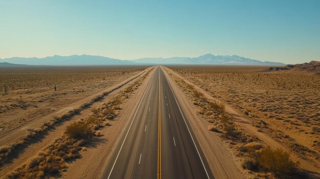 A long straight road stretches through a desert landscape under a clear blue sky