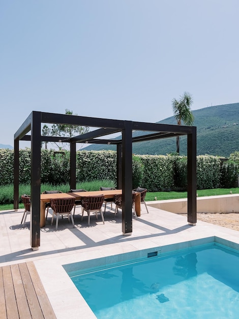 Long table with chairs in a wooden pergola near the pool