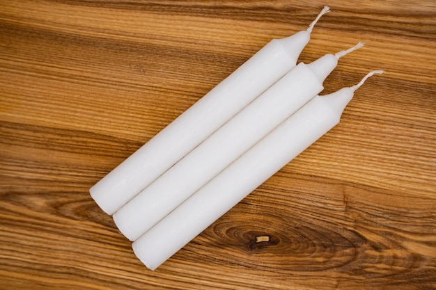 Long wax candles. Three white wax candles on a wooden background. Set of traditional candles