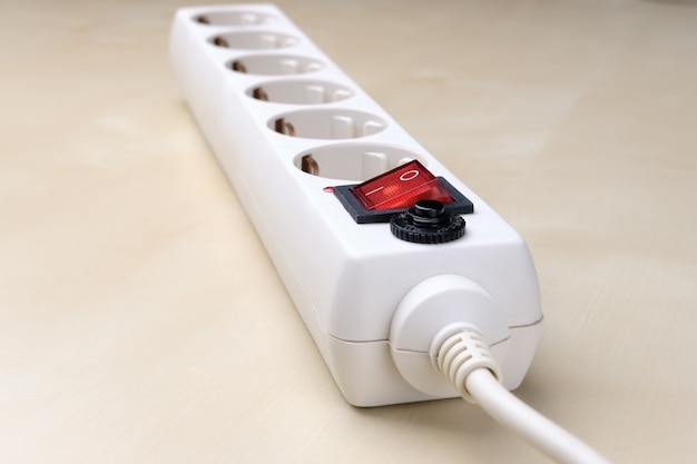 A long white socket-splitter with a bright red button lies diagonally on a light surface and goes into the distance in perspective.