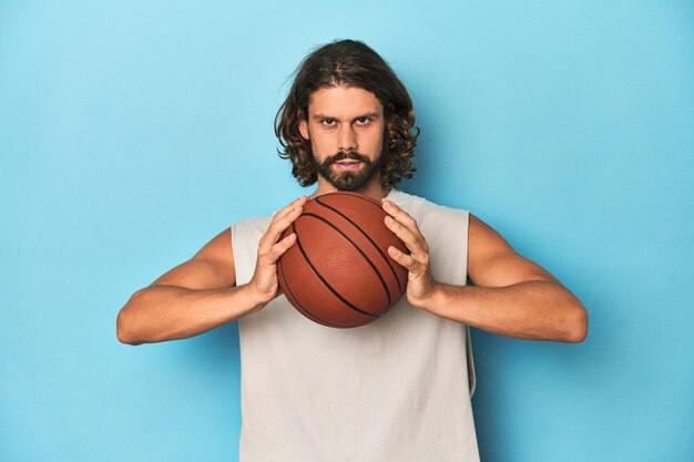 Longhaired bearded man holding a basketball in a blue studio