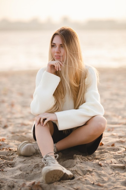 Longhaired blonde girl sitting on the sandy beach in the autumn morning