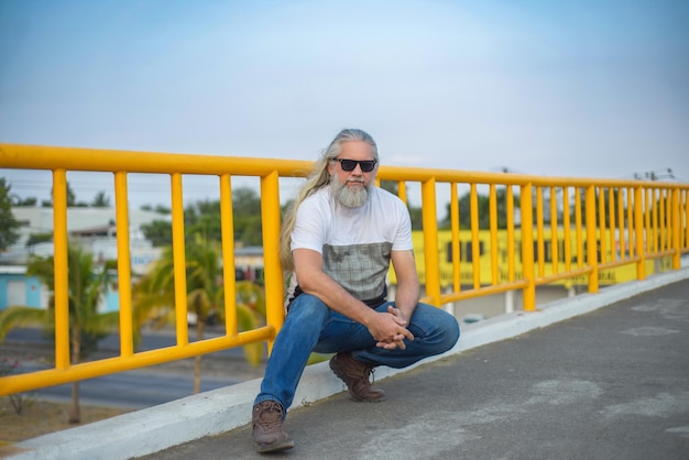 Longhaired grayhaired man wearing dark glasses on a pedestrian bridge Cityscape in the background