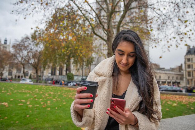 Longhaired indian girl while walking at the park messages and drinks hot tea