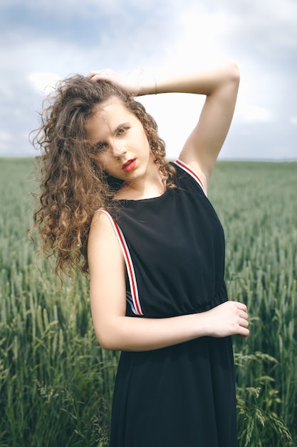 Longhaired pretty girl in black dress standing on the green field