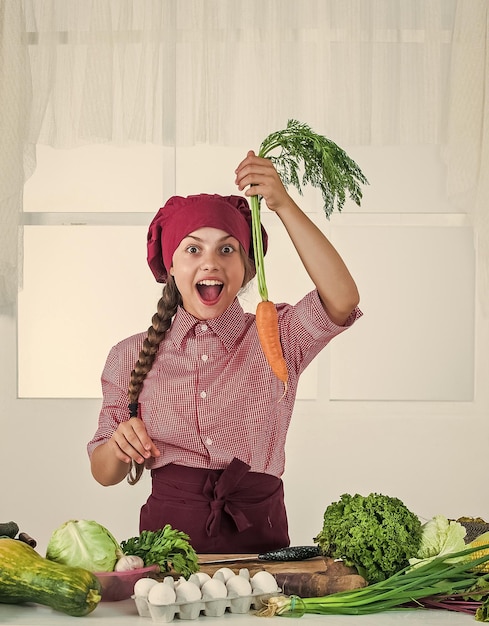 Look at that kid wear chef uniform and hat teen girl preparing carrot fresh raw vegetables time to eat happy child cooking in kitchen healthy and organic food only full of vitamins