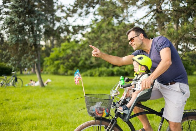 Look over there active family day in nature father and son ride bike through city park on sunny summ