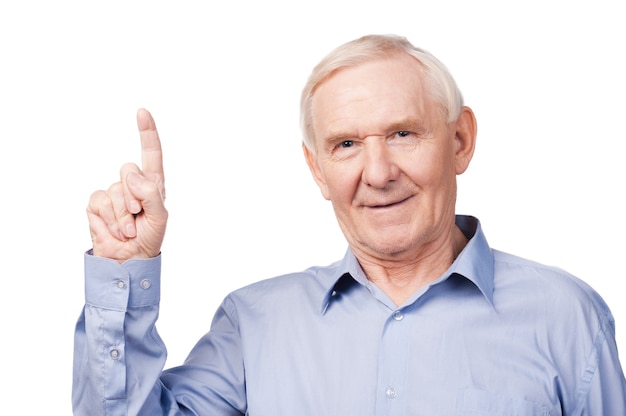 Look over there! Cheerful senior man pointing up and smiling while standing against white background