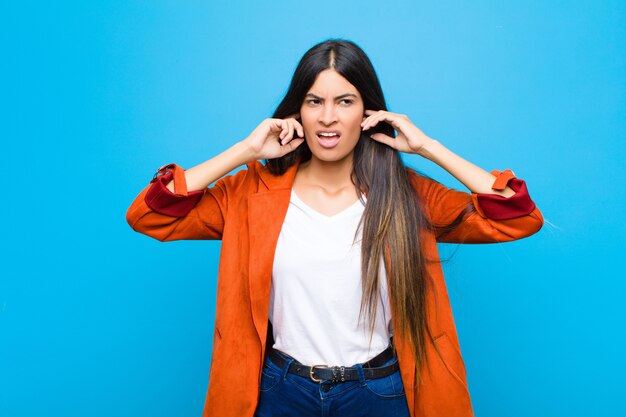 looking angry, stressed and annoyed, covering both ears to a deafening noise, sound or loud music