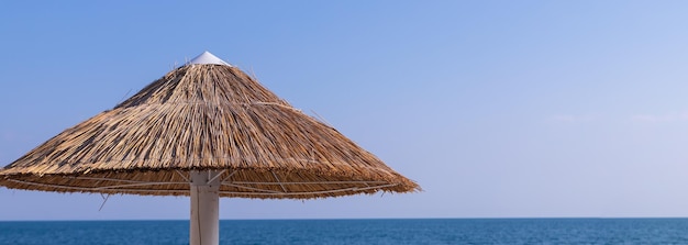 Looking at the blue sea through a straw beach umbrellaStraw umbrellas with sunbeds on the sandy beachBamboo umbrellas blue sky on summer holiday and relax concept